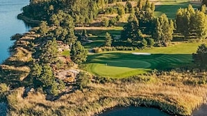 Een golfbaan met een waterpartij aan de ene kant, omgeven door dichte bomen en open grasvelden.
