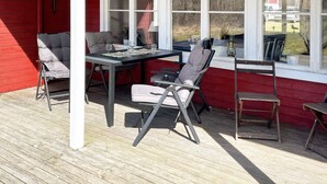 A covered outdoor seating area with a table and chairs, a red building, and a window overlooking a yard. - 4 Star Holiday Home in Askersund (Askersund)
