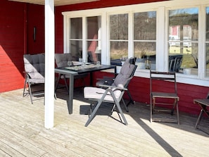 A covered outdoor seating area with a table and chairs, a red building, and a window overlooking a yard. - 4 Star Holiday Home in Askersund (Askersund)