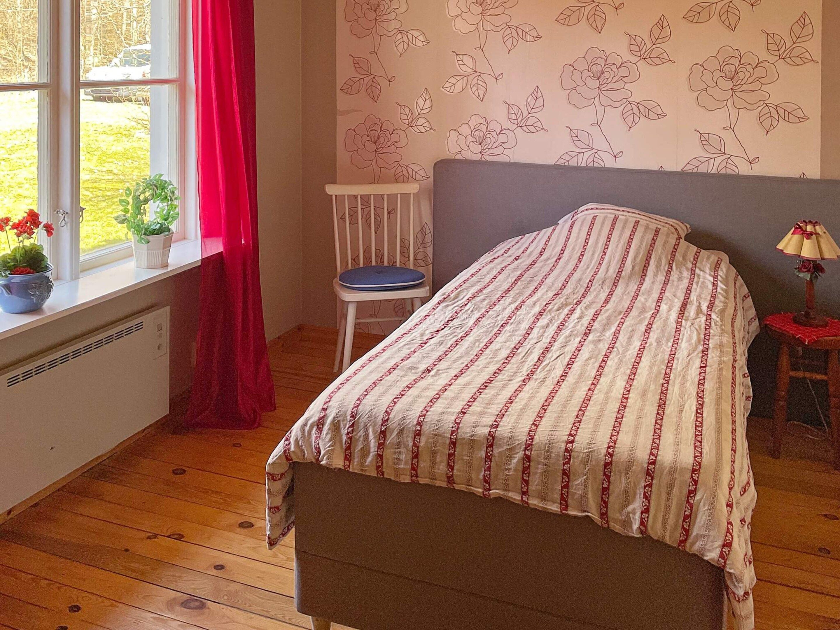 A bedroom with a bed, a chair, a window with curtains, and a radiator.
