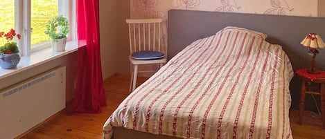 Une chambre à coucher avec un lit, une chaise, une fenêtre avec des rideaux et un radiateur.