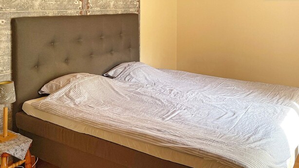 A single bed with a grey headboard and a striped bedspread in a room with wooden flooring and a marble nightstand. - 4 Star Holiday Home in Askersund (Askersund)