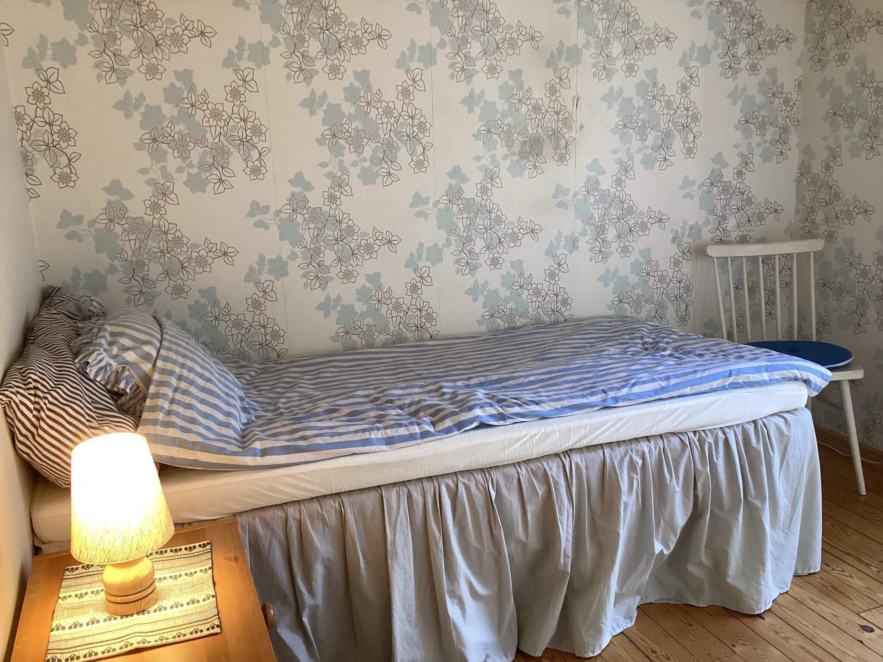 Una cama individual con una colcha a rayas, una lámpara de noche y una silla.