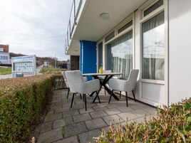 Eine Terrasse mit zwei Korbstühlen und einem Tisch, einer blauen Wand und einem mit Vorhängen drapierten Fenster.