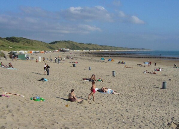 A beach with people sunbathing and walking, tents, and a pier in the background. - Apartment in Zoutelande Near the Beach (Zoutelande)