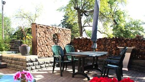 An outdoor patio with a stone wall, green chairs, a round table, and potted plants. - Ferienwohnung in Lichtenhain (Sebnitz)