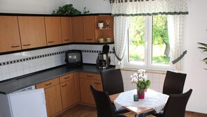 A kitchen with wooden cabinets, a white refrigerator, a coffee maker, and a table with chairs. - Ferienwohnung in Lichtenhain (Sebnitz)