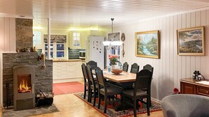 Een gezellige woonkamer met een open haard, een eetgedeelte met een houten tafel en stoelen, en een keuken met witte kastjes en een accentmuur van steen.