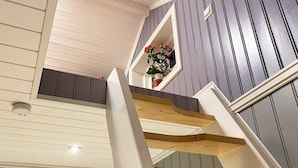 Een houten trap met een witte leuning die uitkomt op een plateau met een klein raam.