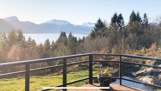 Een houten terras met een leuning, met uitzicht op een meer en bergen.