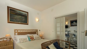A hotel room with a bed, a wicker chair, a dining table with chairs, and a painting on the wall. - Marina di Castagneto Carducci Stay (Castagneto Carducci)