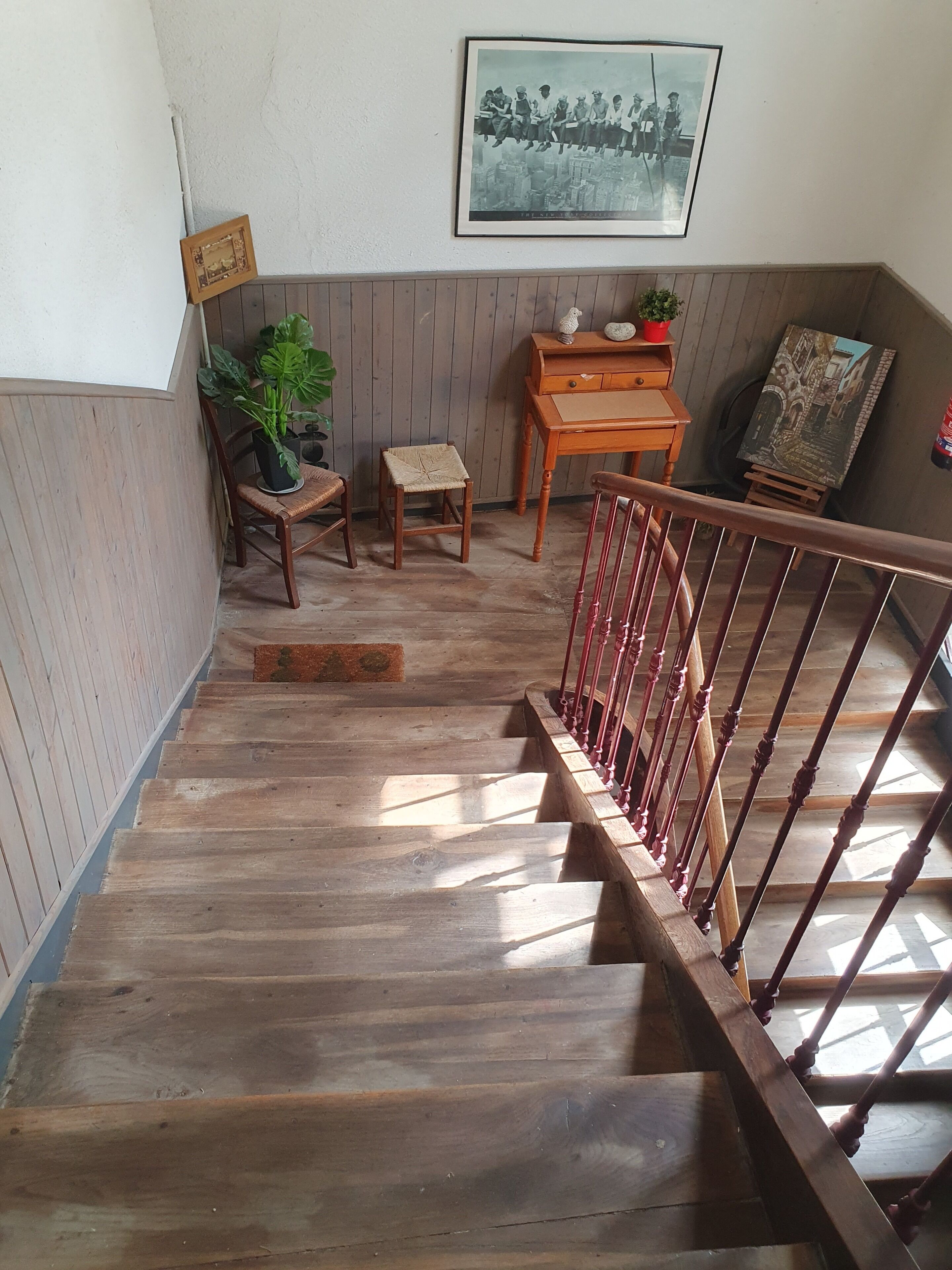 Eine Holztreppe mit roter Geländer, ein gerahmtes Foto an der Wand, ein kleiner Holztisch und ein Blumentopf.
