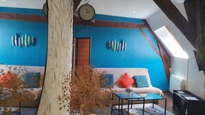 A cozy loft-style living room with a blue accent wall, a wooden ceiling, a large clock, and a sofa with cushions.