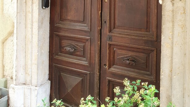 A large wooden double door with a keyhole and a small lock, flanked by two wall-mounted lanterns.