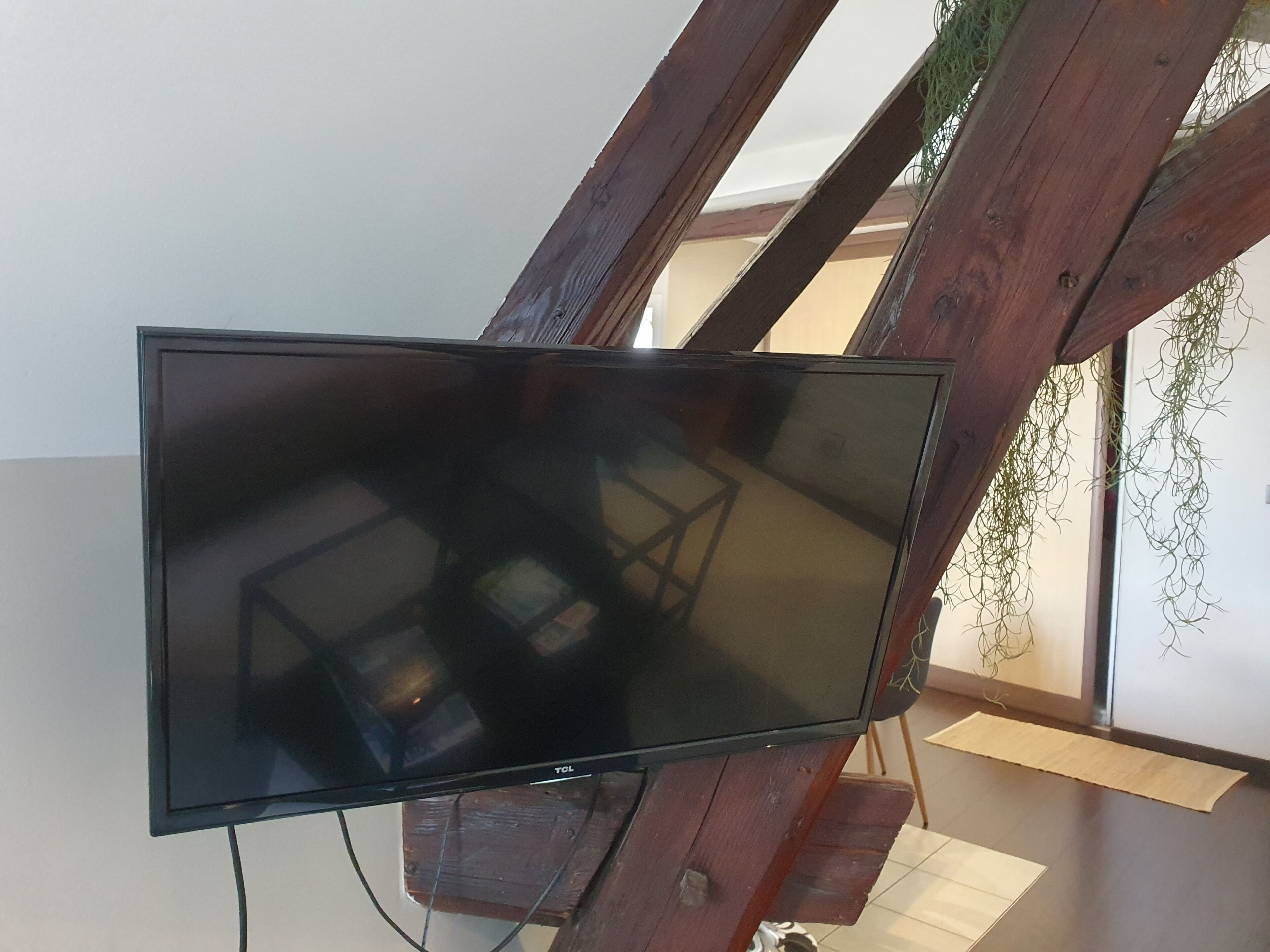 A flat-screen TV mounted on a wooden structure with a window and hanging plants in the background.