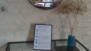 A mirror on a wall with a framed interior regulation sign below it, a glass table with a blue vase, and a brick wall.