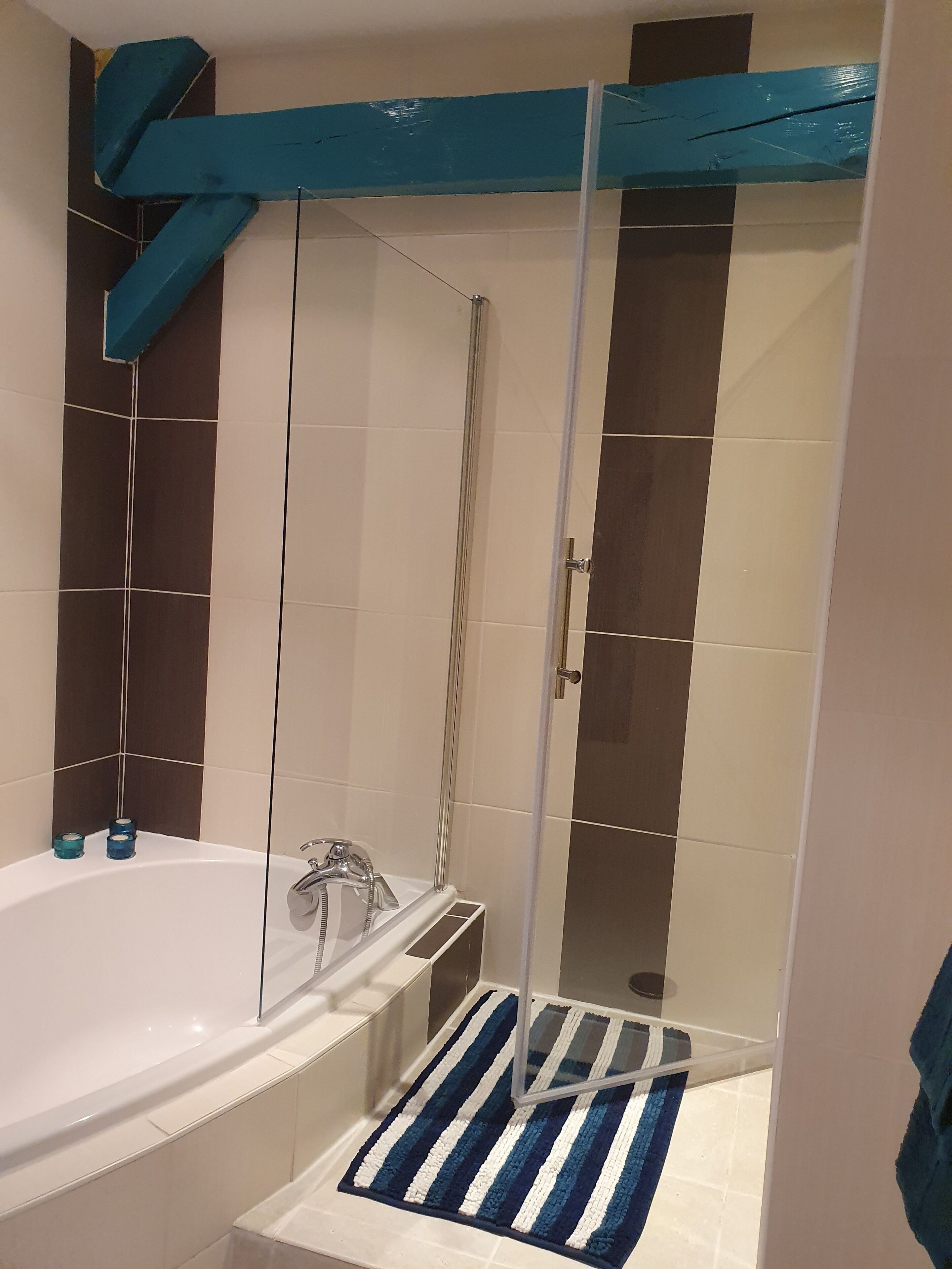 Een badkamer met een badkuip, een douche met glazen wand en een badmat met strepen.