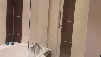 Een badkamer met een badkuip, een douche met glazen wand en een badmat met strepen.