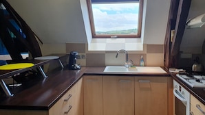 A kitchen with a window, a sink, a stove, and wooden cabinets.
