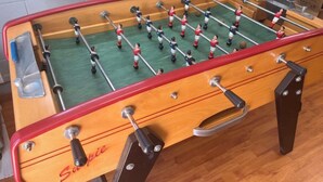A foosball table with a wooden frame, metal rods, and red and white player figures. - Location Villa Juin-juillet (La Possession)