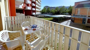 Ein Balkon mit weißen Plastikstühlen und einem Tisch, mit Blick auf einen Parkplatz und Gebäude im Hintergrund.