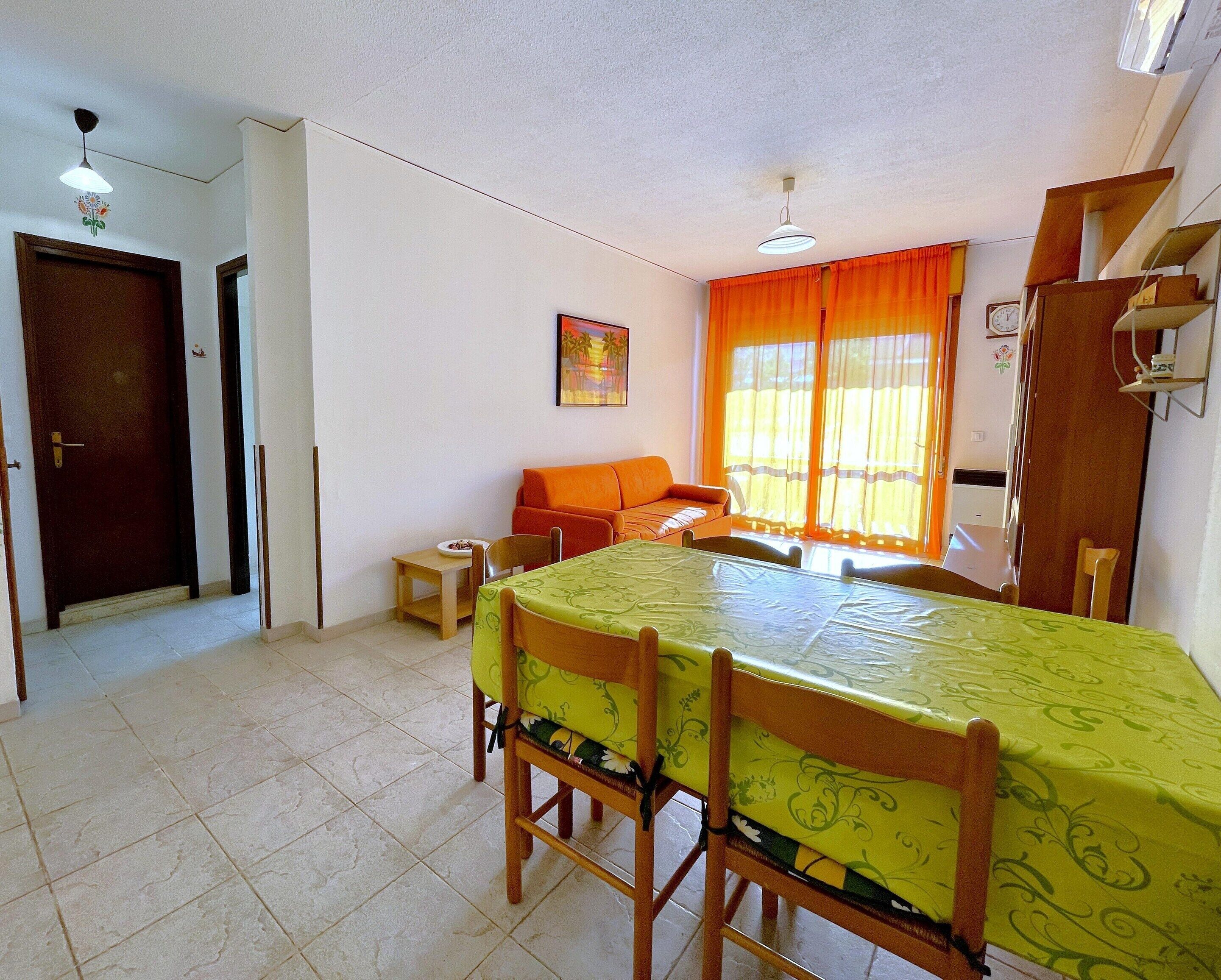 A room with a dining table, chairs, a sofa, and a window with curtains.