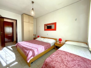 Een slaapkamer met twee bedden, een kledingkast, een spiegel en een plafondlamp.