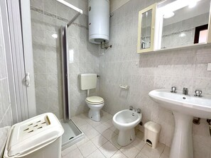 Een badkamer met toilet, bidet, wastafel en douchecabine.