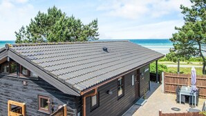 A wooden cabin with a sloped roof, a small porch, and a view of the ocean. - 5 Star Holiday Home in Glesborg (Glesborg)