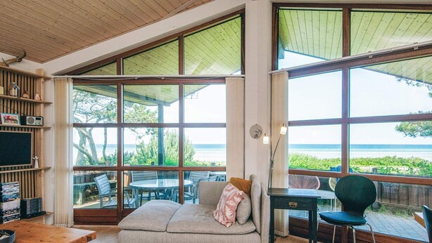 A cozy room with a large window overlooking the sea, a sofa, a small table, and a bookshelf. - 5 Star Holiday Home in Glesborg (Glesborg)