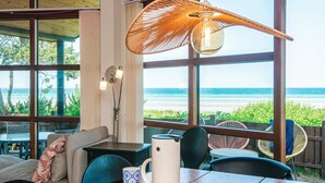 A room with a wooden table, chairs, a sofa, and a large window overlooking the beach. - 5 Star Holiday Home in Glesborg (Glesborg)