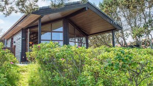 A modern wooden cabin with large windows and a covered porch, surrounded by lush greenery and trees. - 5 Star Holiday Home in Glesborg (Glesborg)