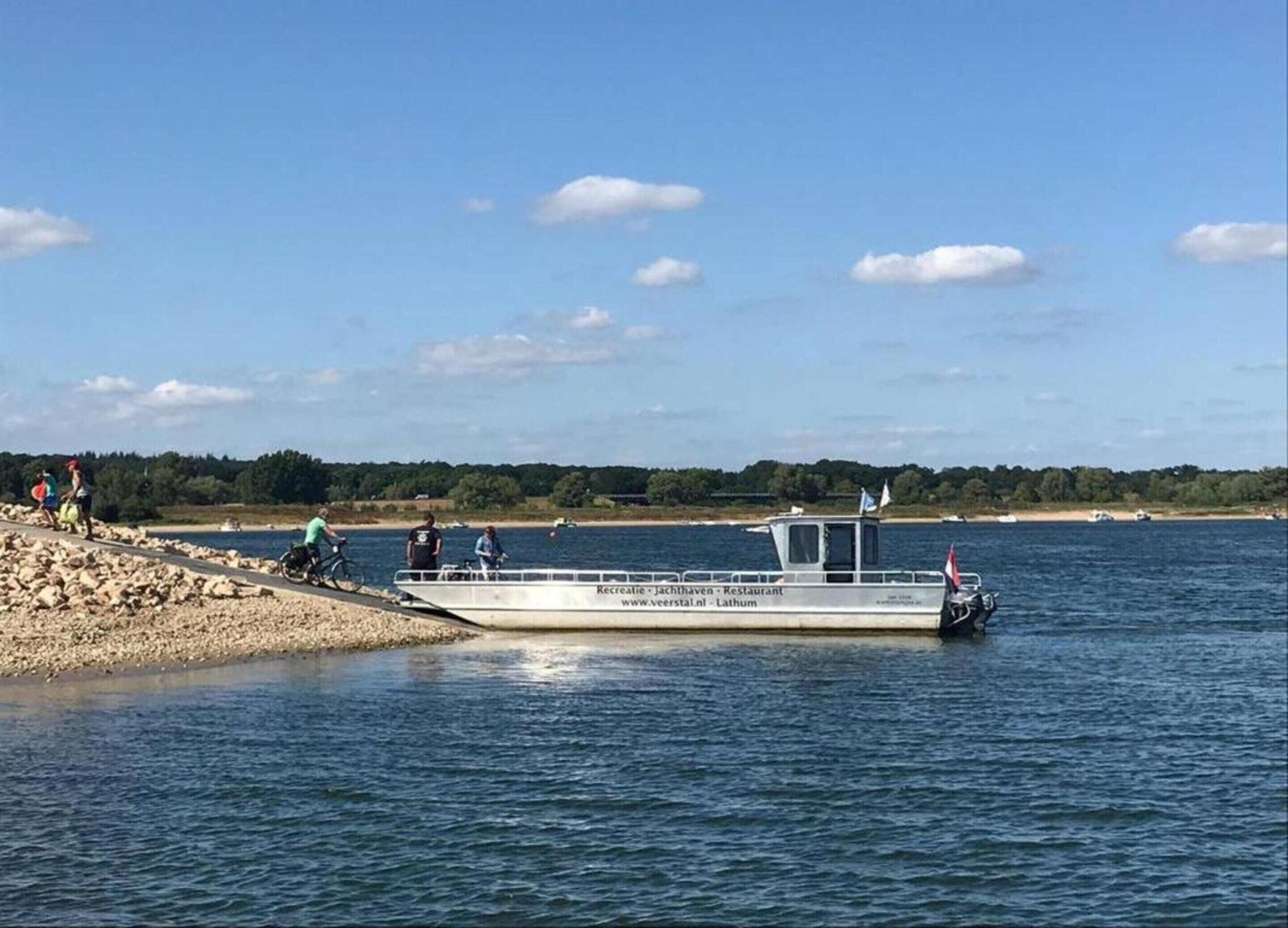 A boat docked at a rocky shore with people walking and cycling nearby.