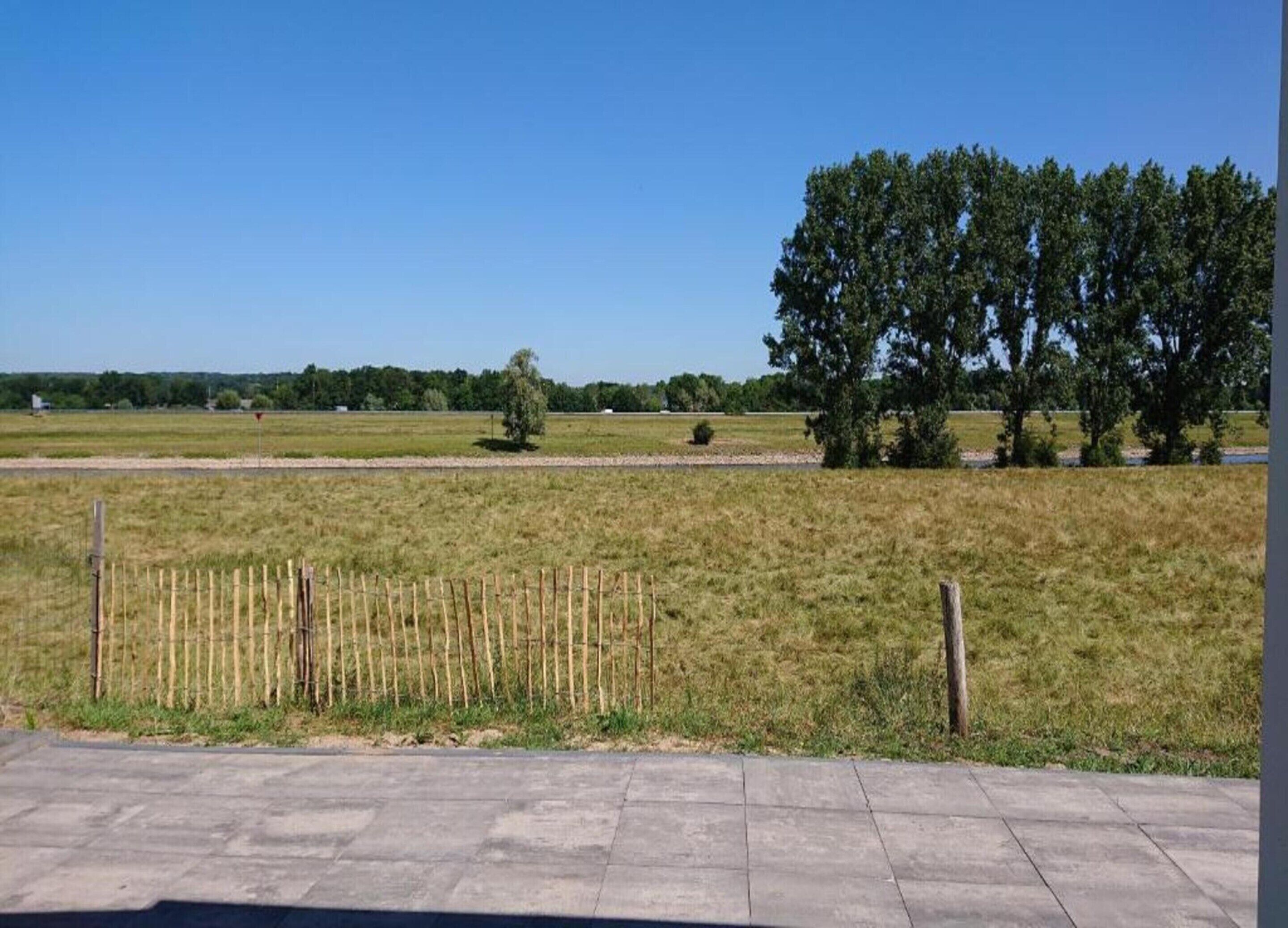 Un paysage rural avec un ciel dégagé, une zone délimitée par une clôture et quelques arbres.