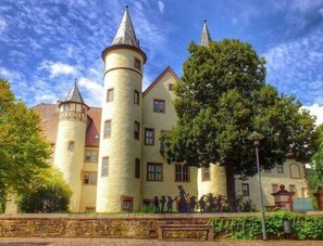 Un edificio parecido a un castillo con múltiples torres y un árbol grande en primer plano.