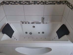 Eine weiße Badewanne mit zwei schwarzen Fußstützen, einer fest installierten Duschbrause und einem Ablauf.
