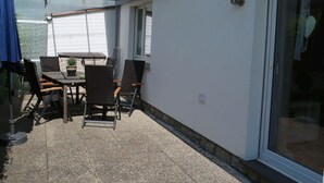 Ein überdachter Patio-Bereich mit Tisch und Stühlen, einem Blumentopf und einer Schiebetür.