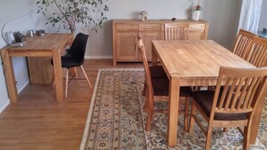 Ein Essbereich mit Holztisch und -stühlen, einem Teppich, einer Pflanze und einer Küchenzeile mit Schränken und einer Pendelleuchte.