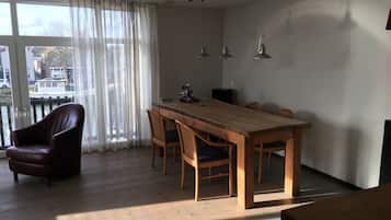 A dining area with a wooden table and chairs, a leather chair, and a view through large windows.