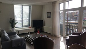 Un salon comprenant un canapé, une table basse, un téléviseur et un balcon offrant une vue sur les immeubles.
