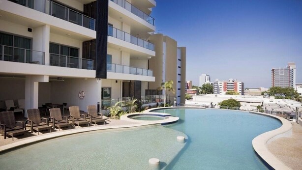 A modern hotel with a pool area, lounge chairs, and a view of the city skyline. - Hotel Style Room in the heart of Darwin  (Darwin City)