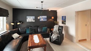 A modern living room with a black leather sofa, a wooden coffee table, and a black armchair. There are two wall-mounted lamps and a painting above the sofa. - 4 Star Holiday Home in Helgeroa (Larvik)