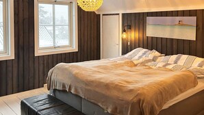 A bedroom with a bed, a bench, a hanging light fixture, a painting, and a window. - 4 Star Holiday Home in Helgeroa (Larvik)