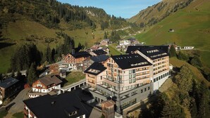 Ein dörfliches Bergidyll mit traditionellen Holzhäusern und modernen Gebäuden, umgeben von üppigem Grün und blauem Himmel.