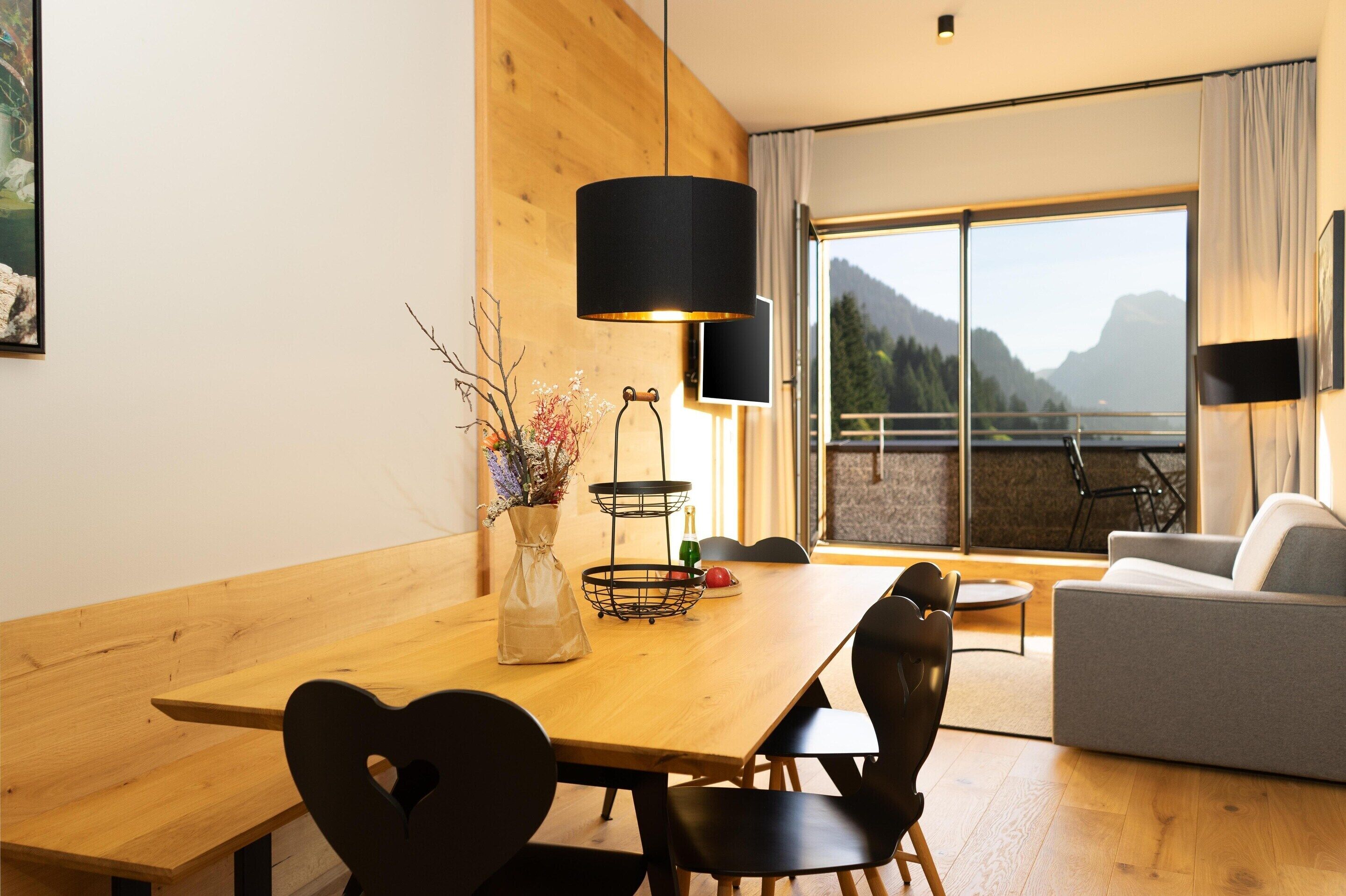 Un espace repas moderne avec une table en bois, des chaises noires et un vase rempli de fleurs.