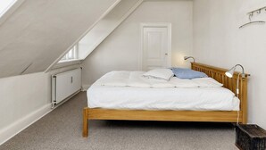A bedroom with a sloped ceiling, a bed with white bedding, a wooden headboard, a bedside lamp, and a radiator. - 4 Star Holiday Home in Faaborg (Faaborg)