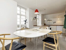 A modern kitchen with white cabinetry, a dining table with chairs, and a red pendant light.