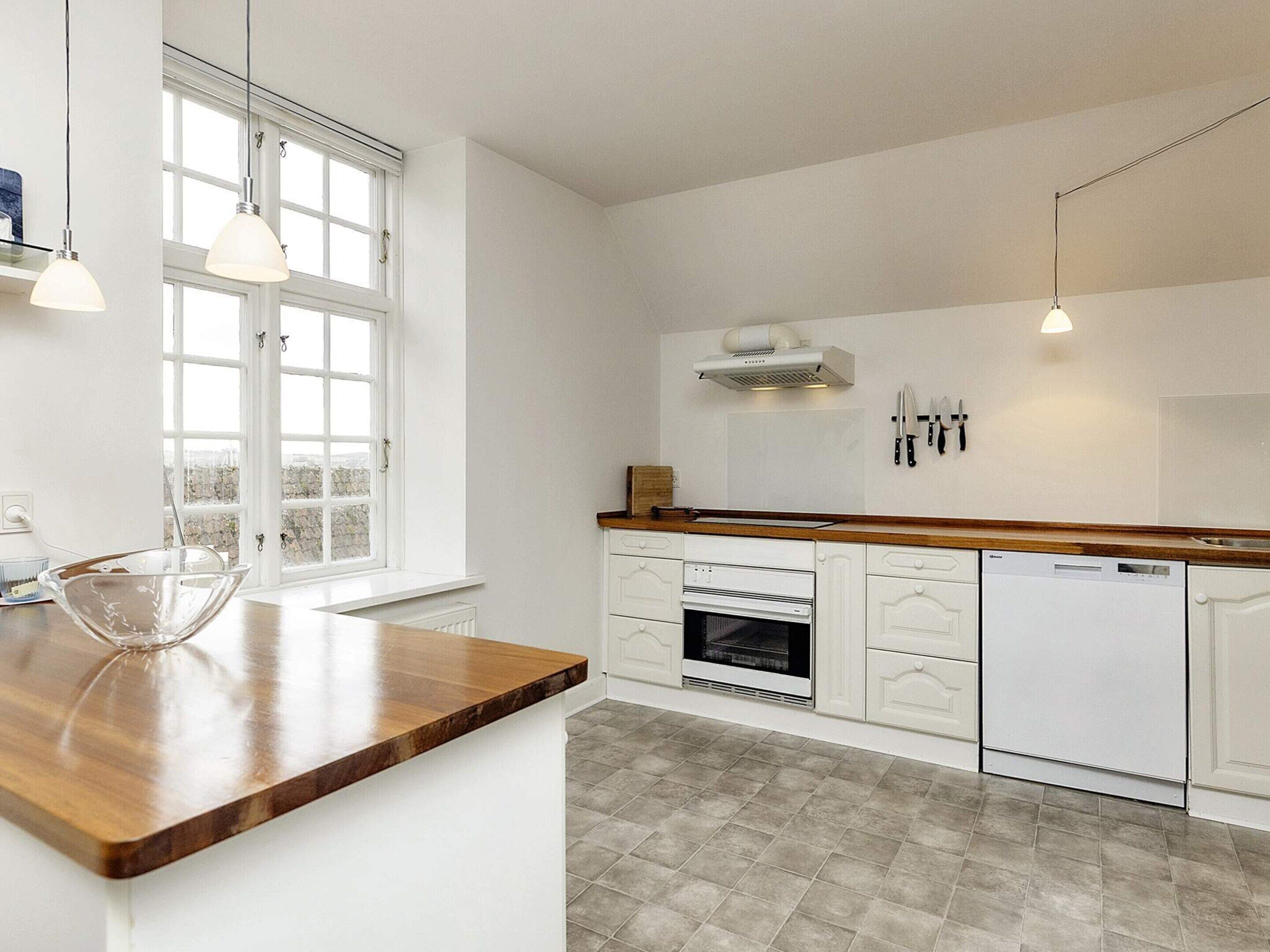 Ett modernt kök med vita skåp, en bänkskiva i trä, en inbyggd ugn och en diskmaskin.