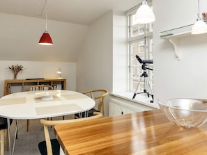 A dining area with a round table, chairs, a red pendant light, a telescope on a tripod, and a window with a view of buildings. - 4 Star Holiday Home in Faaborg (Faaborg)