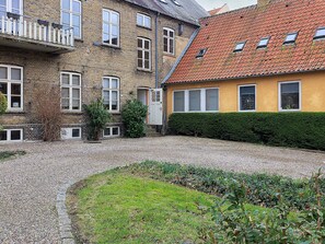 A courtyard with a gravel path, a small garden area, and a building with a brick facade and a yellow wall. - 4 Star Holiday Home in Faaborg (Faaborg)